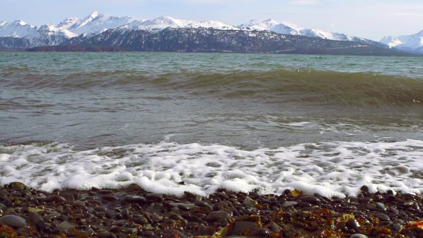 Slow motion dolly shot left of waves rushing in Land's End Beach in Homer,