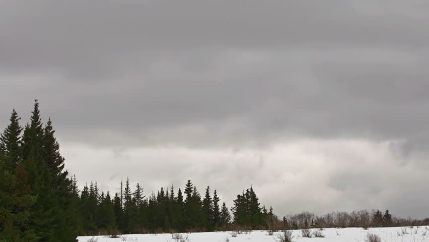 Slower timelapse of massive brooding storm clouds moving across snowy ridge and
