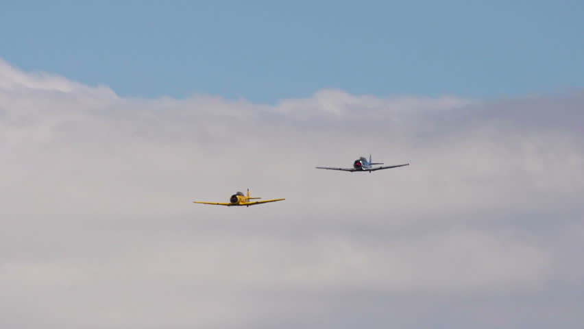 Two vintage restored World War 2 aircraft fly in staggered formation in a cloudy