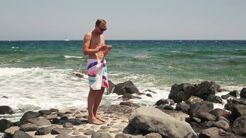 Man in trunks taking photo with cellphone by the sea
