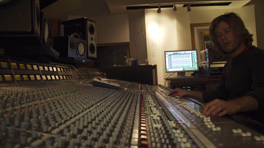 A young studio engineer working at a large SSL mixing board in recording studio.