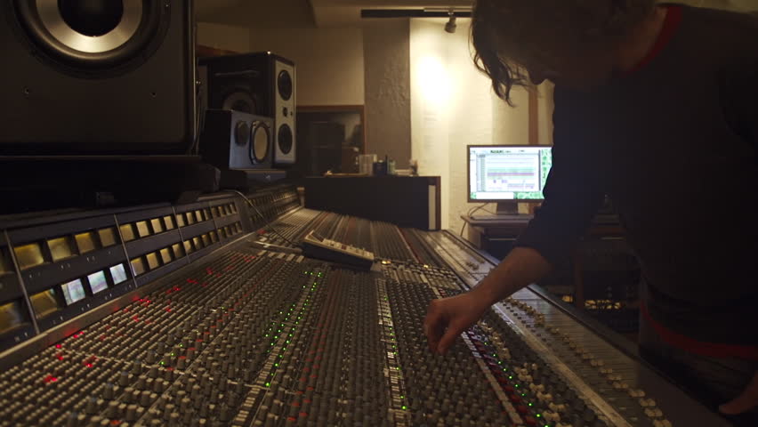 Young audio recording professional adjusts large mixing board in recording