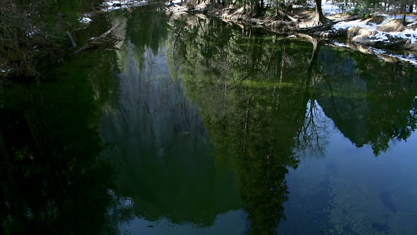 Reflections of trees, granite, and sky in the calm waters of the Merced River in