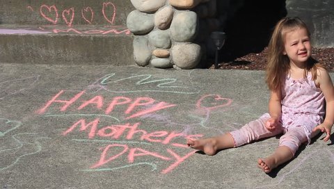 A child writes a mothers day message on the sidewalk with chalk.