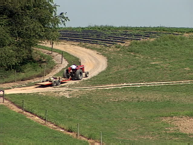 A farmer rides his tractor up a hillside on his farm.