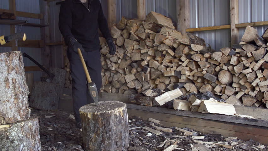 Alaskan man splits firewood inside woodshed with an ax