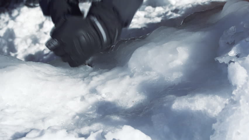Mountaineer cuts handholds into the vertical face of a frozen cliff with an ice
