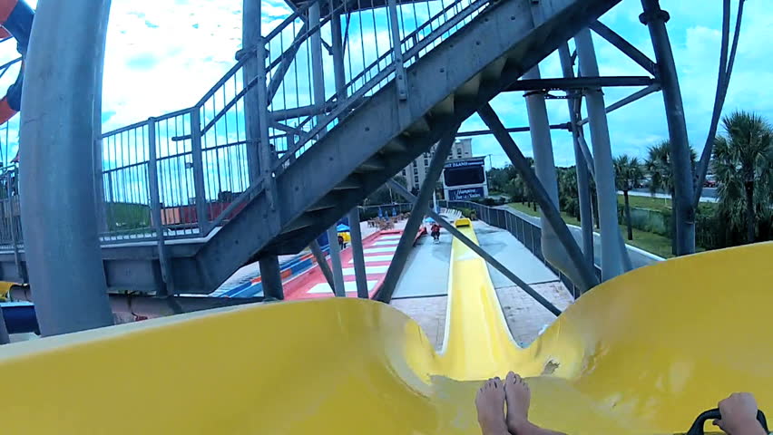 Point of view legs feet young girl as she slides down plastic chute at water park