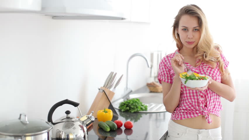 Pretty young woman in kitchen eating vegetable salad
