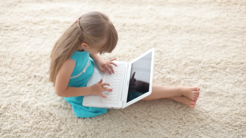 Cute little girl sitting on floor using laptop and smiling at camera
