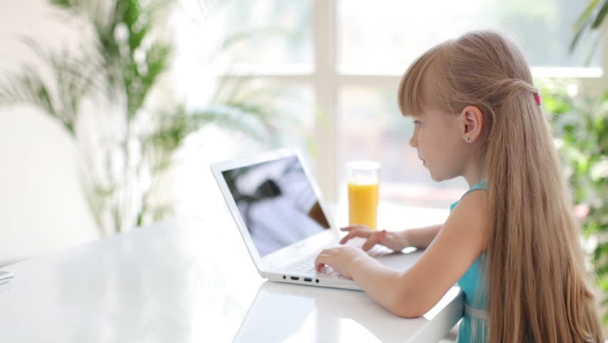 Cute little girl sitting at table using laptop turning around and looking at