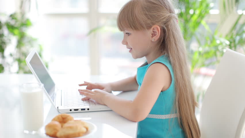 Adorable little girl sitting at table with laptop smiling and laughing at