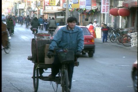 BEIJING - FEBRUARY 09, 1999: Man rides three-wheeled flatbed bicycle through street