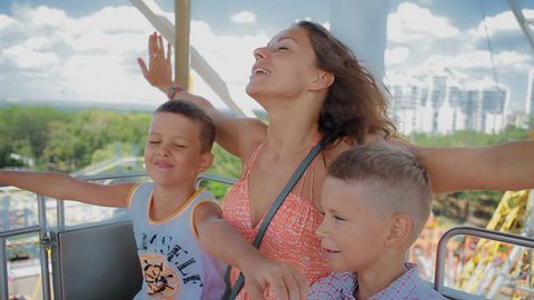 mom with two kids ride on the Ferris wheel. They pretend that fly and look very cheerful and happy