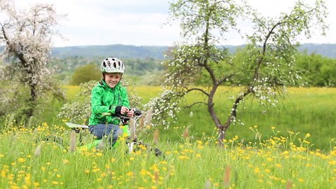 Boy stands with his bike in a summer meadow and tells a story