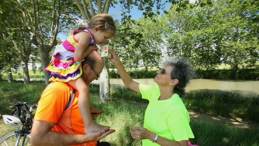 Grandma and grandfather carrying grand daughter on shoulders in nature in summer