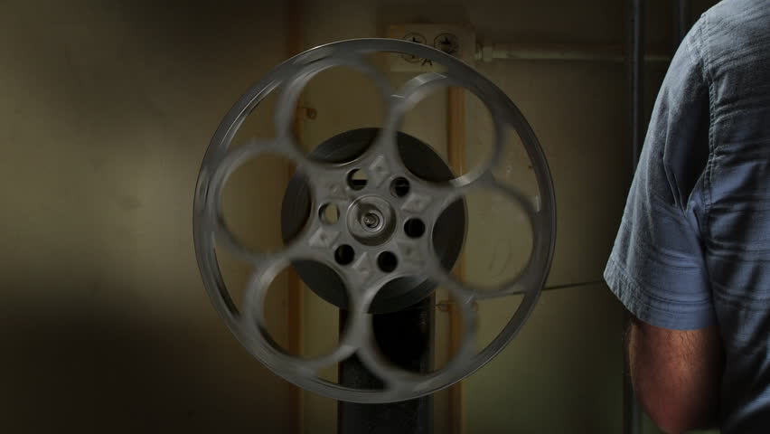 35mm film reel spinning in front of a grungy wall in a projection booth. 