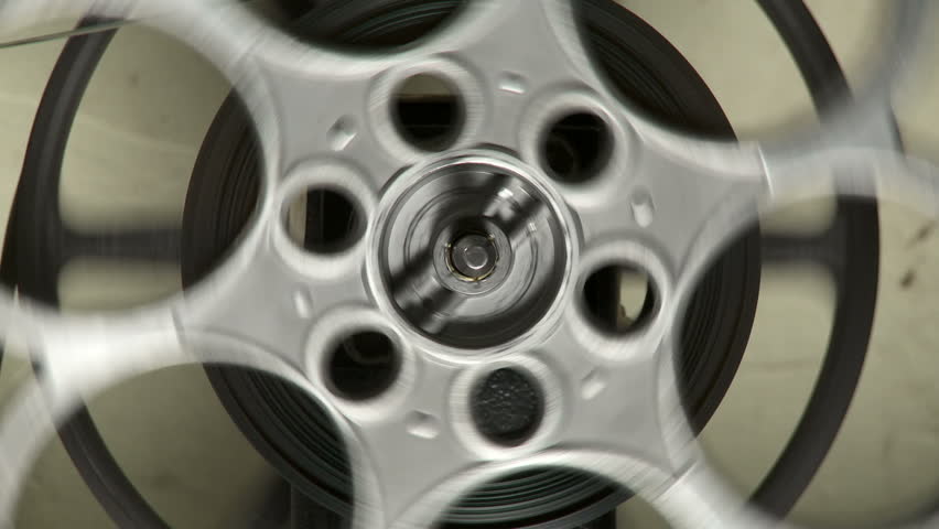 Close up of a 35mm film reel spinning in front of a grungy wall in a projection