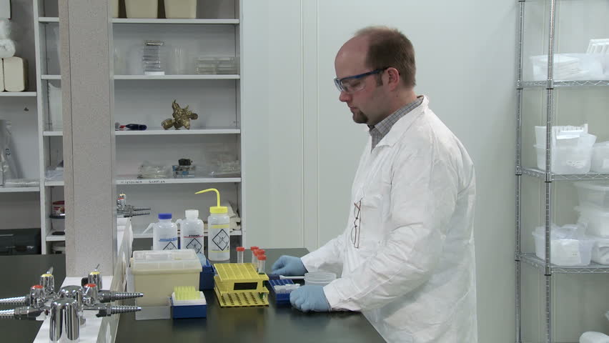 Male scientist working in a laboratory, pipetting liquid and inspecting results.