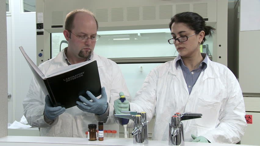 Researchers working in a laboratory, pipetting liquid and making notes in a