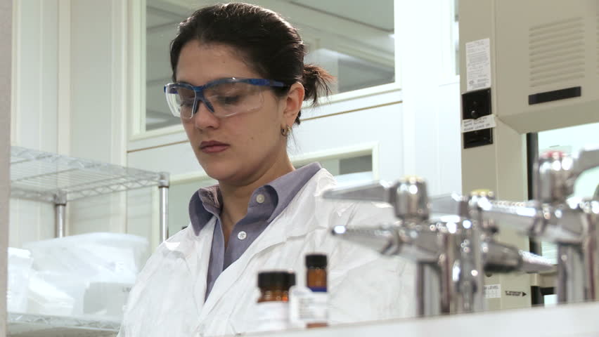 Close up on woman working in a laboratory, wearing safety goggles and pipetting