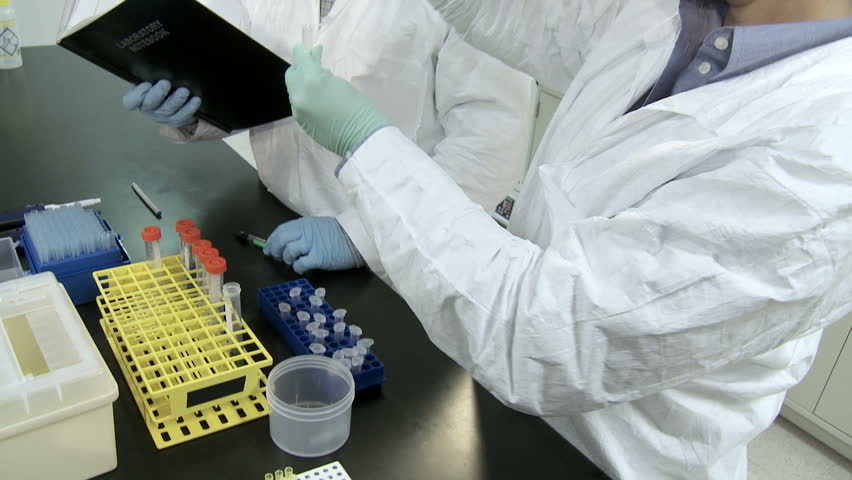 Researchers working in a laboratory, pipetting liquid and noting results in