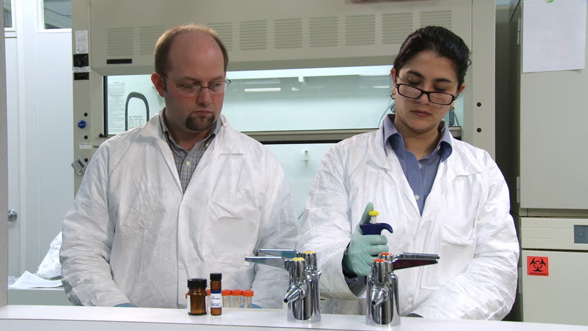 Researchers working in a laboratory, pipetting chemicals and inspecting results.