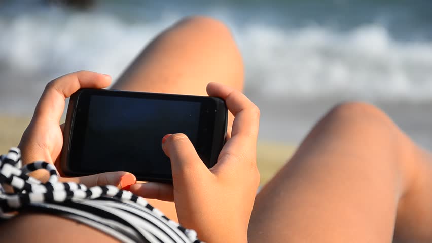 Young girl using a Smartphone on a beach. Fingers touching and swiping the