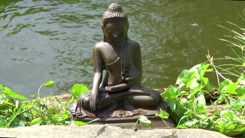 A seated statue of Buddha sits by a pool 