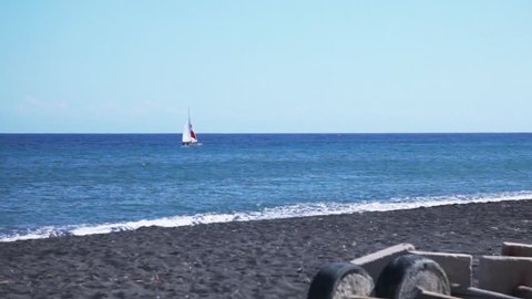 Black sand beaches. Passing yacht. SANTORINI. GREECE