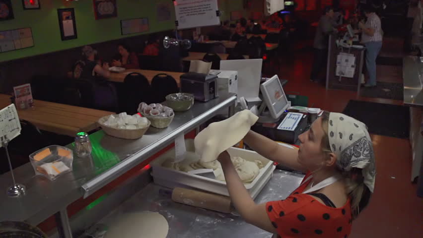 A young woman tosses pizza dough in slow motion in a pizzeria 