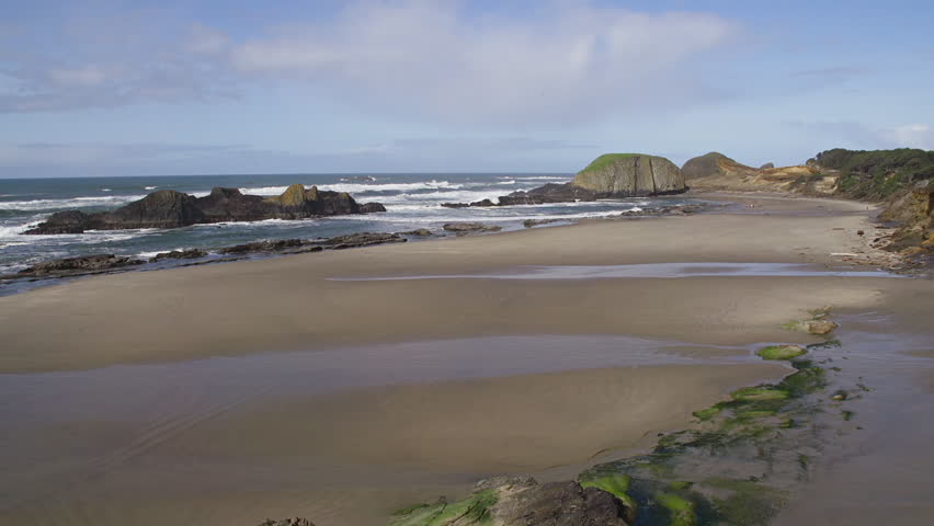 Pacific Ocean tides flow gently against rocks and sand on Seal Rock Beach near