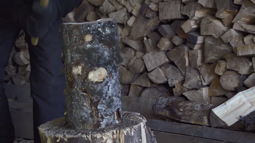 Man in snow pants splits a cord of firewood with an ax in slow motion 