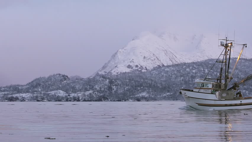 Homer, AK - JANUARY 2013 - Alaskan fishing boat passes snow-capped mountains on 