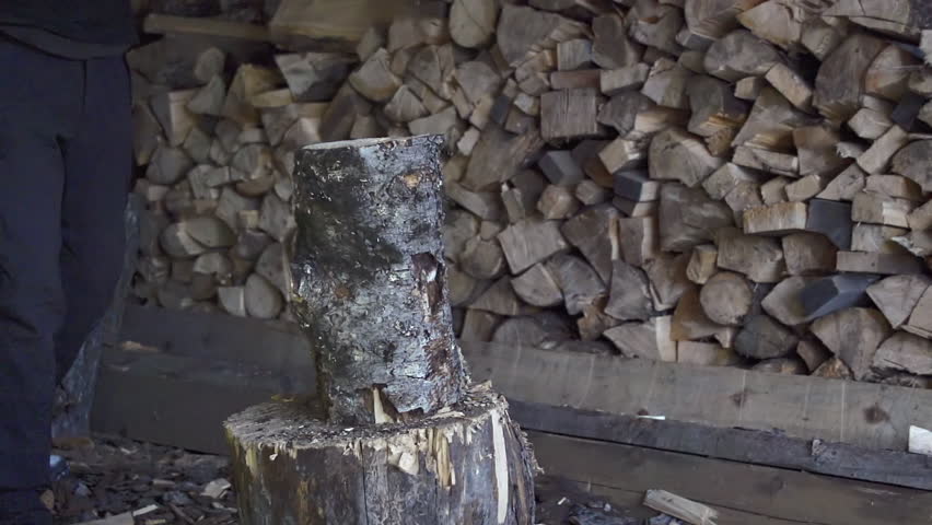 Man splits a length of spruce firewood with an ax in a wilderness wood shed in