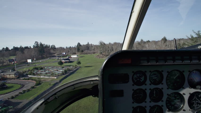 View from passenger seat of a helicopter as it flies past trees in an undefined