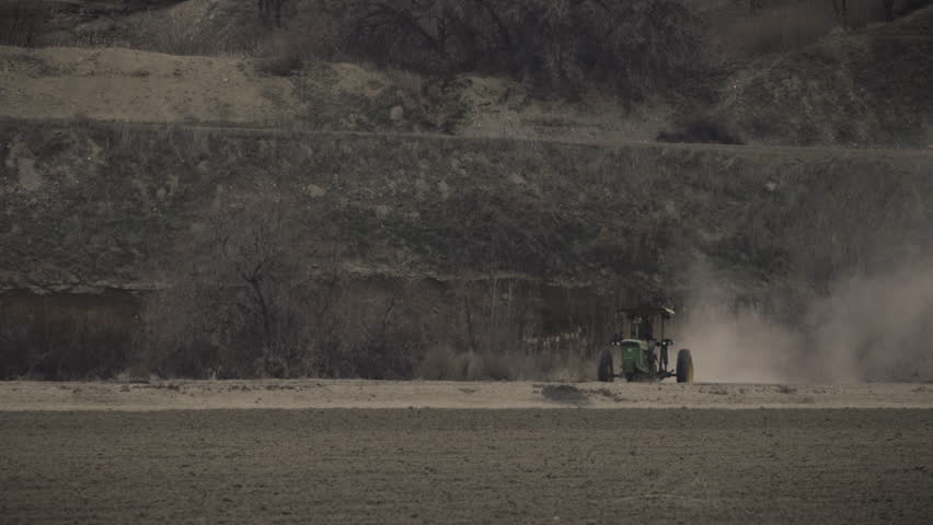 A farmer executes a turn in an old tractor, trailing heavy dust in his wake