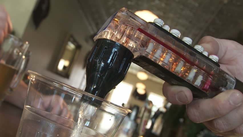 Close up on hand operating a fountain soda dispenser at a bar.  Filling glass