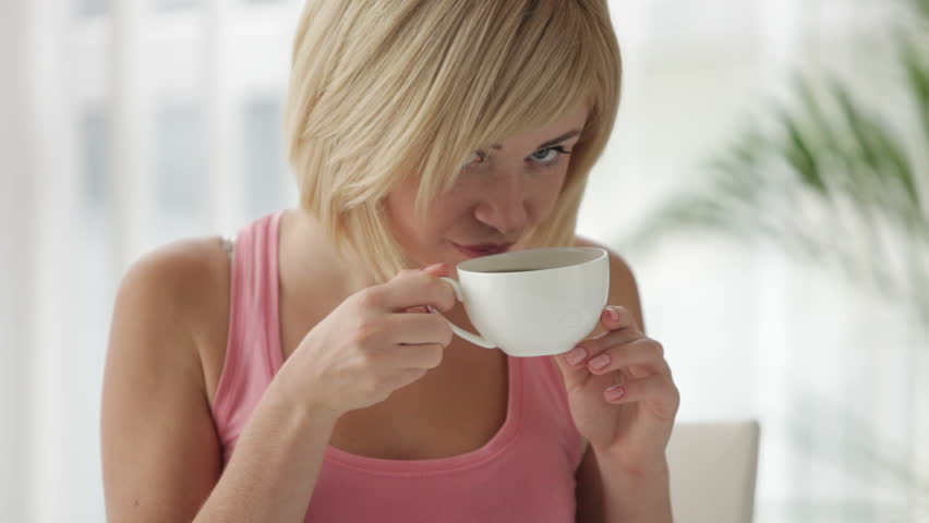 Attractive young woman drinking tea using touchpad and smiling at camera
