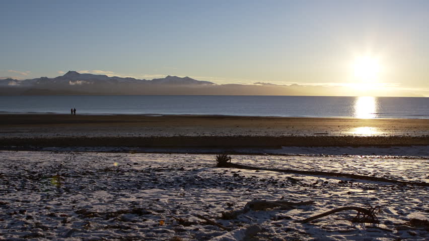 Couple in silhouette walks slowly together alone shoreline of Kachemak Bay at