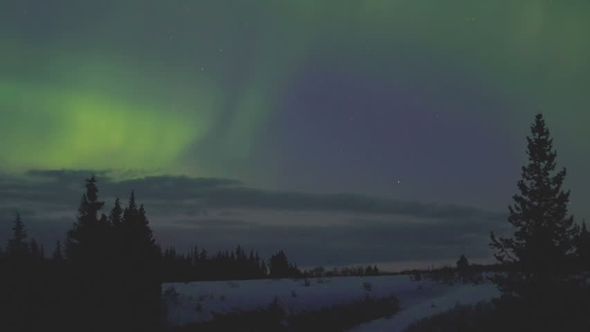 Aurora borealis time lapse lights over snowy landscape and forest in Alaska