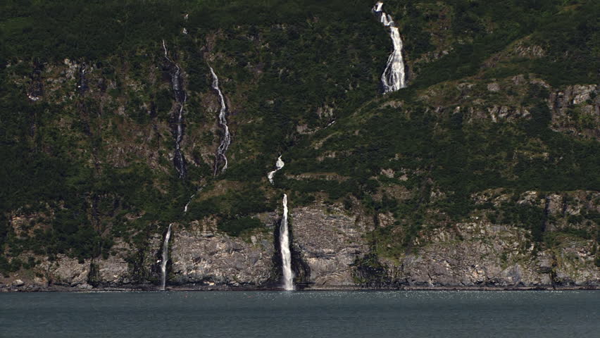 Flock of seagulls swarm on a bay in front of scenic waterfalls tumbling down the