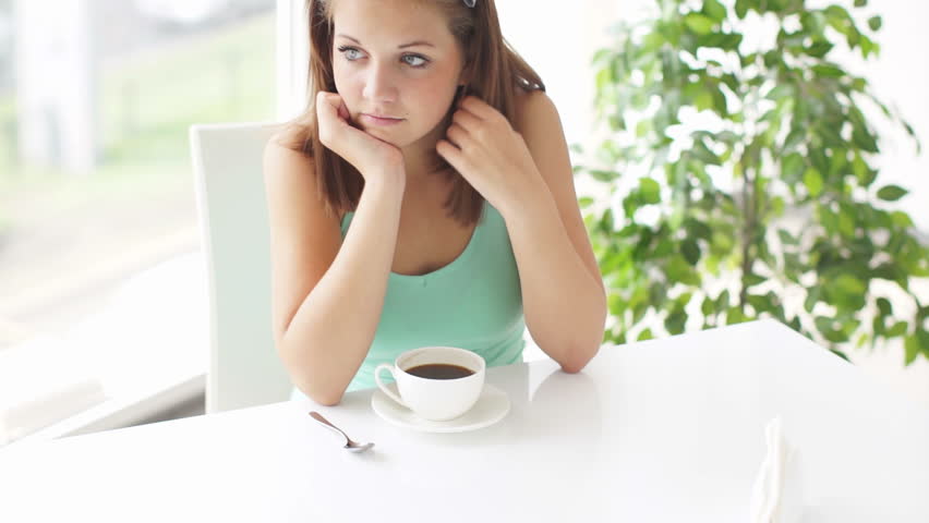 Pretty girl sitting at table drinking coffee smiling and laughing at camera
