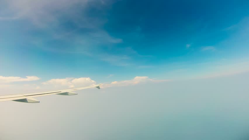 View of blue sky and wing of plane flying through clouds, Time Lapse 
