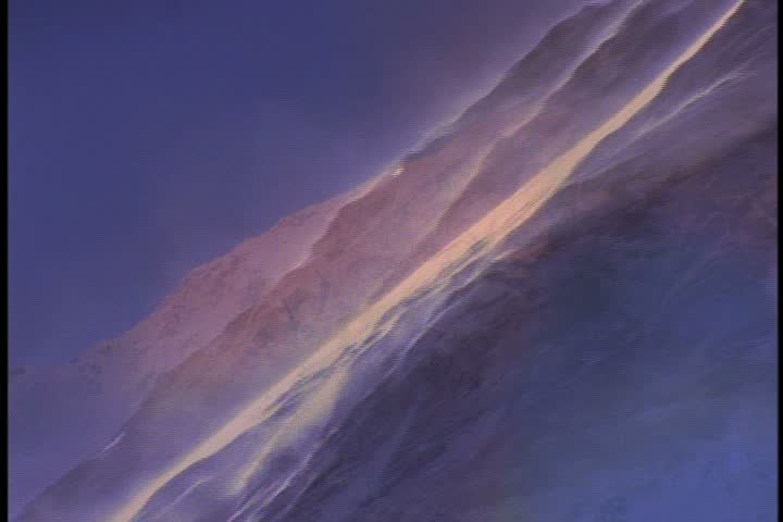 Steep diagonal slope of mountain with blowing, swirling snow in Nepal. Camera tracks up slope.