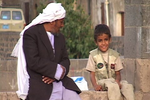 SANA'A, YEMEN - OCTOBER 23, 2002: A Muslim man and his son sitting on a wall, laughing and talking together.