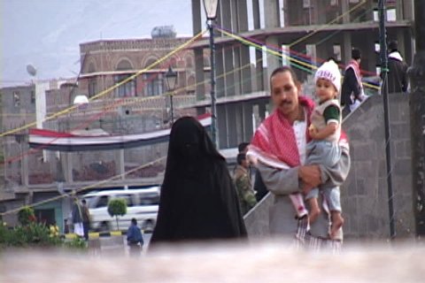 SANA'A, YEMEN - OCTOBER 23, 2002: Muslim man carries child, his wife is following close behind dressed in full black niqab.
