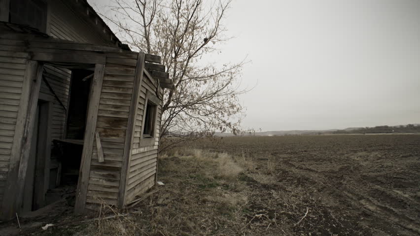 View of a fallow unplowed dirt field to the dilapidated rear porch of an old