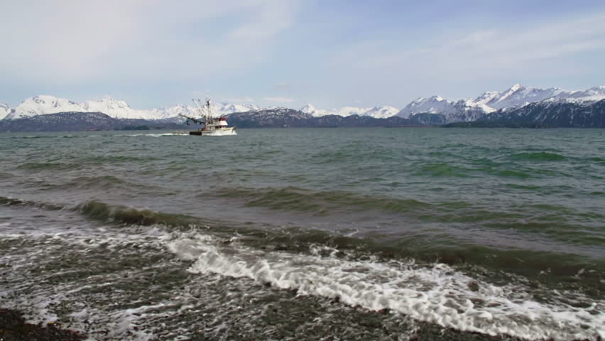 A small Alaskan fishing trawler sails across the tide in front of the stunning