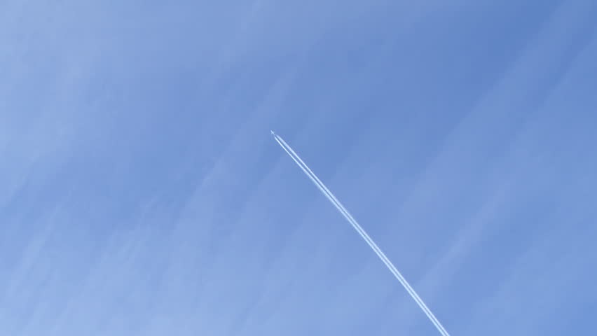 A distant airplane passes high overhead, leaving a jet contrail against a wispy